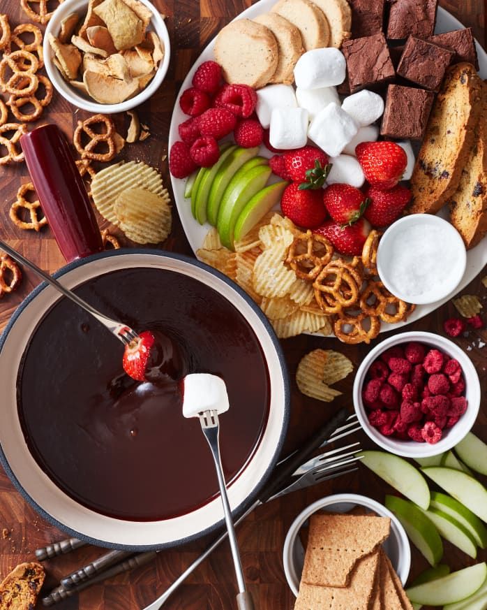 a platter filled with fruit, crackers, and chocolate dip surrounded by pretzels