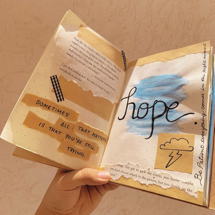 a hand holding an open book with torn paper and writing on the pages that read hope