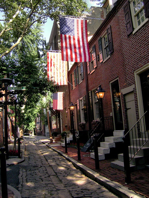 an american flag is hanging from the side of buildings on a brick street lined with trees