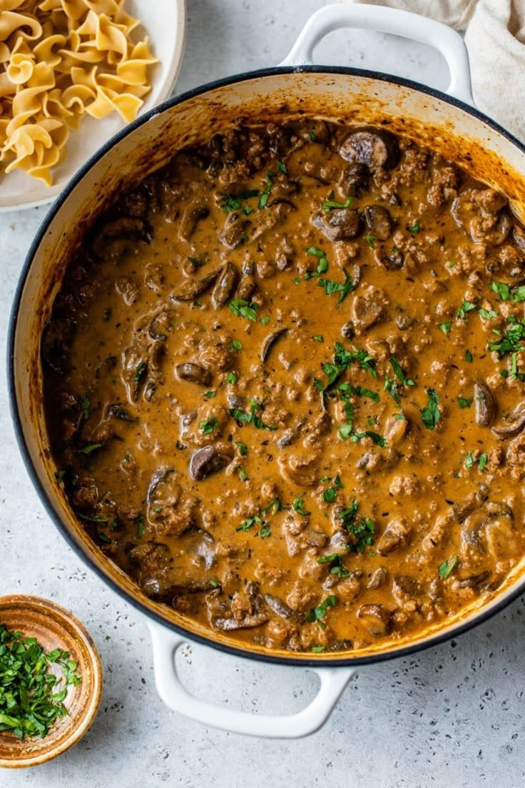 a large pot filled with meat and sauce next to some pasta on the side,