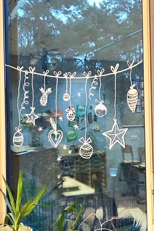 a window decorated with christmas ornaments hanging from it's side and surrounded by potted plants