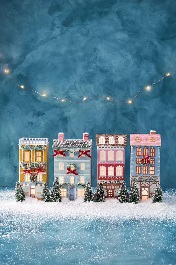 a group of small houses sitting on top of a snow covered ground next to christmas lights