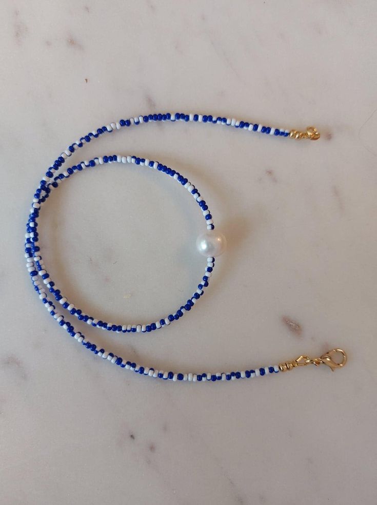 a blue and white beaded lanyard with a gold cross charm on a marble surface