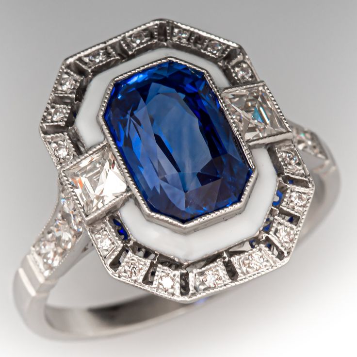 This fabulous Art Deco inspired ring is centered with one (1) cut-cornered rectangular cut natural sapphire that is bordered with white enamel. The ring is accented with two (2) square French cut diamonds, and twenty-two (22) bead set round brilliant and old European cut diamonds. The ring is bordered with milgrain edging. It measures 16.2mm at the top, rises 6.8mm above the finger, tapering to 1.9mm wide and 1.1mm thick at the base of the shank. It is currently a size 7. Blue Sapphire Engagement Ring Art Deco, Heirloom Sapphire Ring With Diamond Cut In Platinum, Art Deco Platinum Sapphire Ring, Luxury Art Deco Sapphire Ring With Polished Finish, Luxury Art Deco Sapphire Ring In Platinum, Antique Platinum Sapphire Ring With Diamond Cut, Blue Engagement Ring, Traditional Diamond, Sapphire Engagement Ring Blue