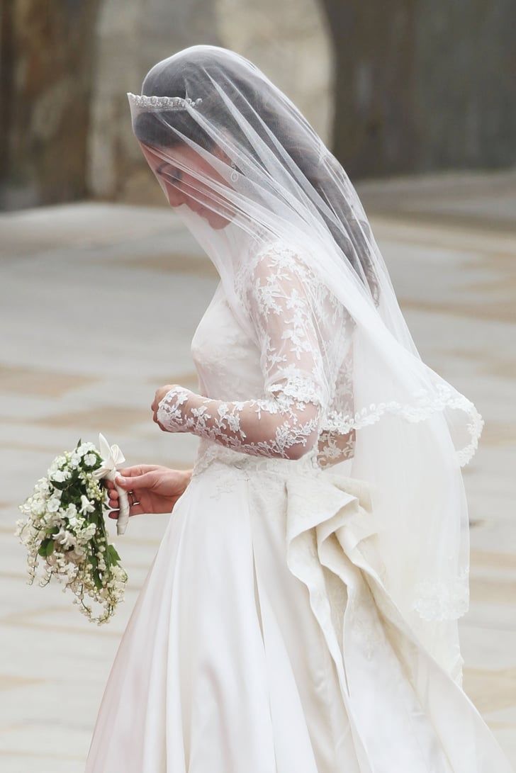 the bride is walking down the street in her wedding dress and veil with flowers on it