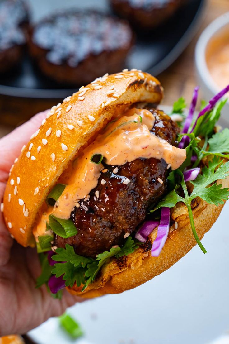 a hand holding a hamburger with meat, lettuce and sauce