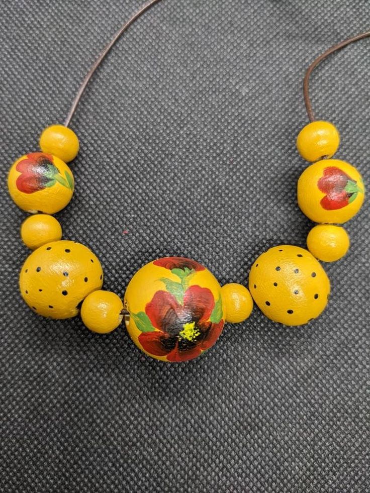 a necklace with yellow beads and flowers painted on the bead is sitting on a gray surface