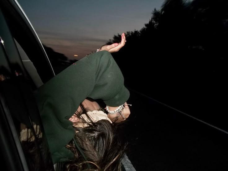 a woman leaning out the window of a car at night with her hands in the air