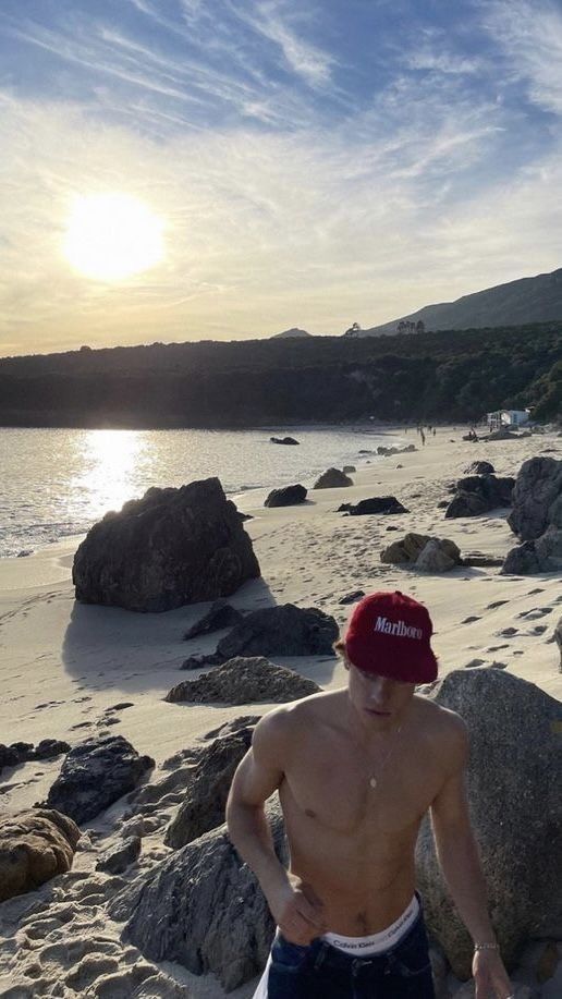 a man standing on top of a sandy beach next to the ocean with rocks in front of him