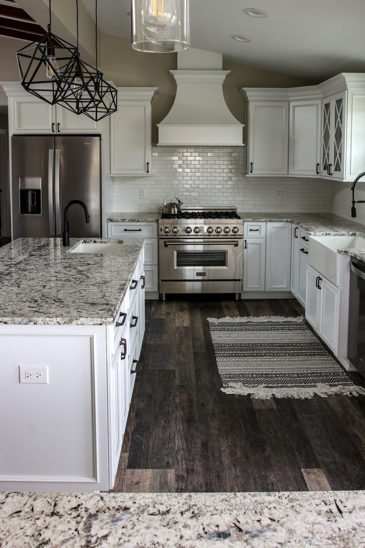 a kitchen with white cabinets and marble counter tops, stainless steel appliances and an island