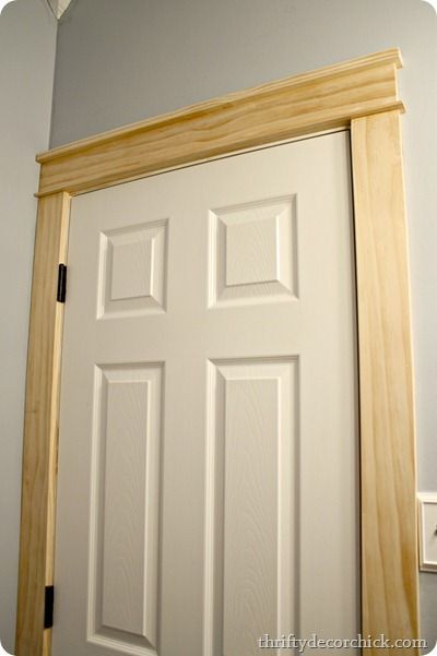 a white door with wooden frame in front of a gray wall and light fixture on the ceiling