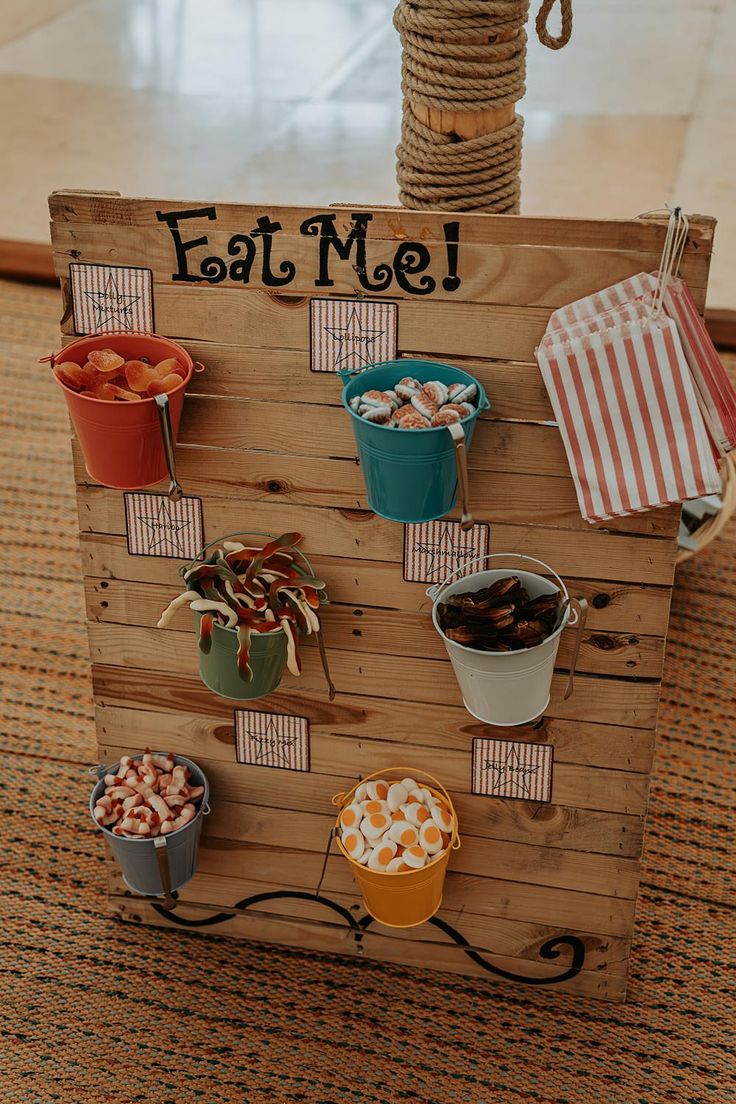 a wooden sign that says eat me with many different foods on it and some candy in buckets