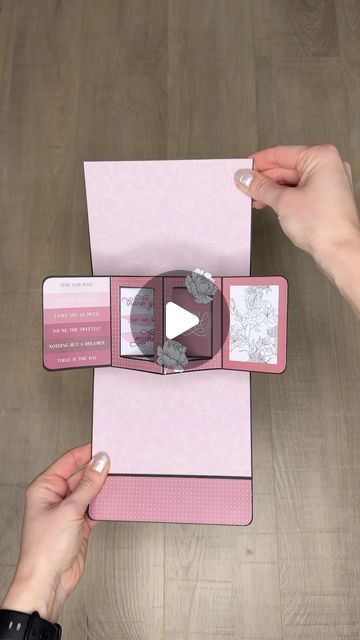 two hands holding an open pink book on top of a wooden table