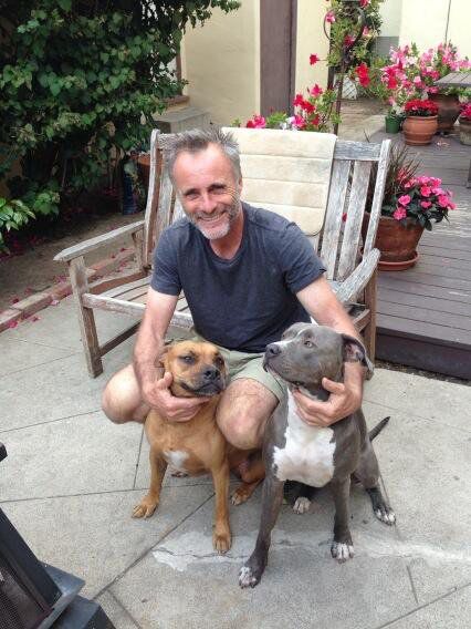 a man sitting on a chair with two dogs in front of him and smiling at the camera