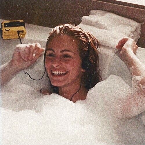 a woman in a bathtub with foam on her head and earphones attached to her ears