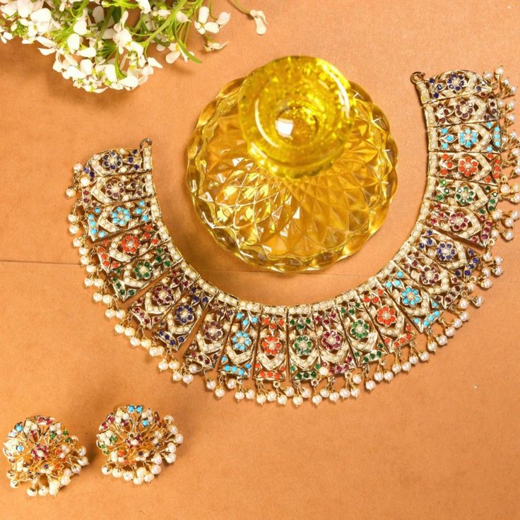 Featured is a traditional bridal Navratan necklace with a matching pair of round studs. The metal is gold plated sterling silver and the stones comprise precious freshwater pearls and a mix of real and synthetic navratan colored stones. The approximate Weight of the necklace is 60 GMs and the weight of the earrings is 15 gms. Hand Set Pearl Necklace In Temple Style, Temple Style Pearl Necklace Hand Set, Hand Set Pearl Temple Necklaces, Multicolor Necklace With Intricate Design For Ceremonial Occasions, Hand Set Pearl Necklaces Temple Style, Ceremonial Multicolor Necklace With Intricate Design, Elegant Multicolor Necklaces For Ceremonial Occasions, Fusion Style Bridal Necklace With Round Tilla, Festive Pearl Jewelry With Meenakari