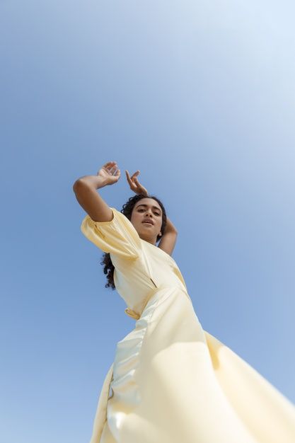 a woman in a yellow dress is reaching up into the air with her hands and arms