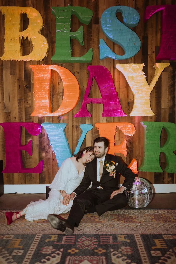 a bride and groom sitting on the floor in front of colorful letters