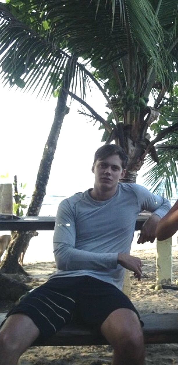 two men sitting on a bench under a palm tree