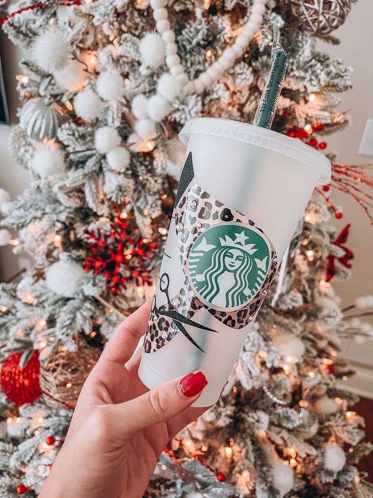 a woman holding up a starbucks cup in front of a christmas tree with red and white ornaments