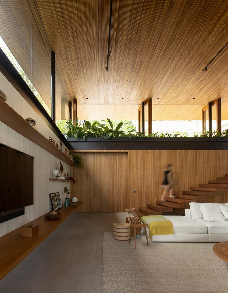 a living room with wooden walls and stairs leading up to the top floor, while a person is walking in the distance