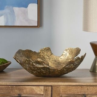 a wooden table topped with a metal bowl next to a lamp and painting on the wall