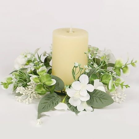 a white candle surrounded by flowers and greenery