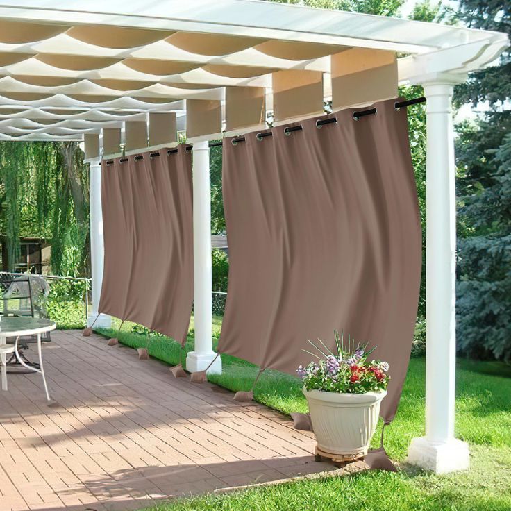 a patio covered with curtains and chairs in the grass next to a wooden deck surrounded by trees