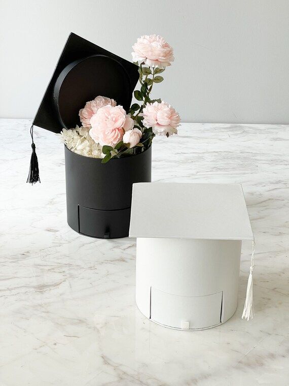 a white box with flowers in it and a black hat sitting on top of it