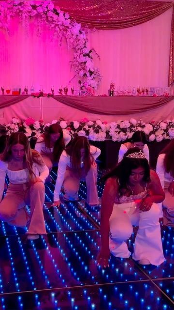 a group of women in white dresses dancing on a dance floor with blue and pink lights