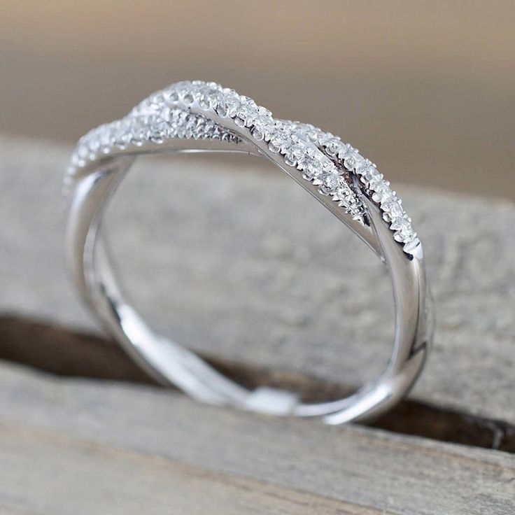 a white gold wedding ring with diamonds on the top and bottom, sitting on a piece of wood