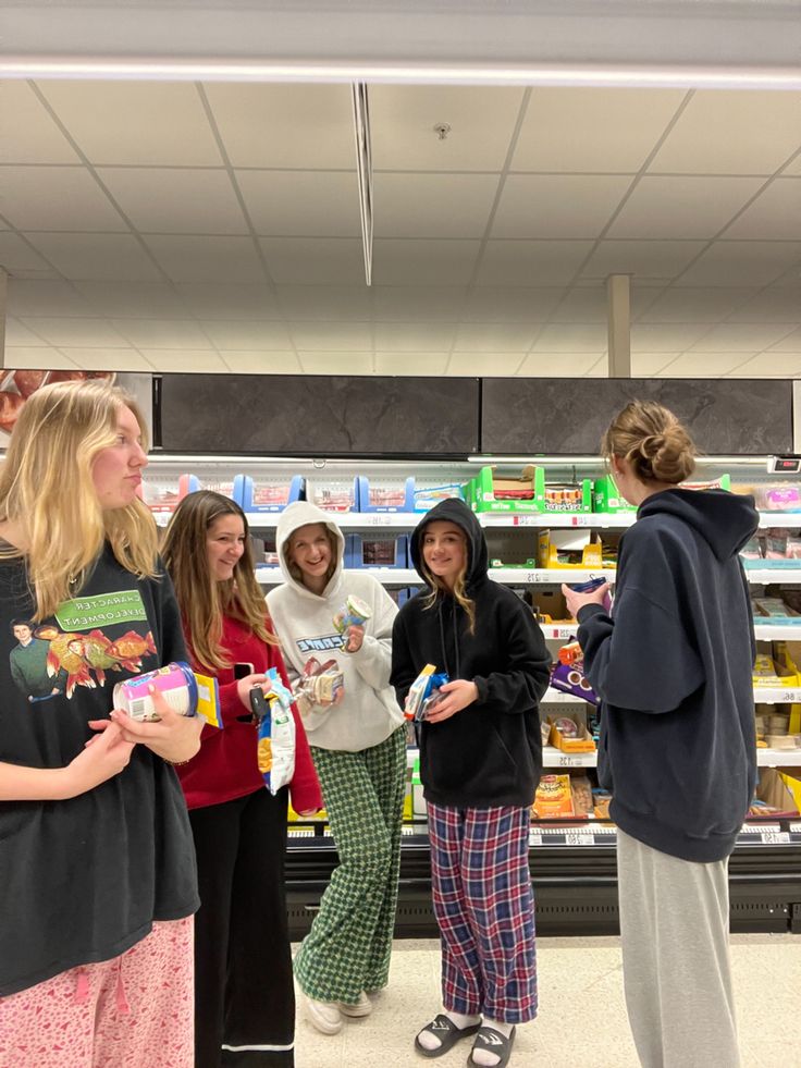 four girls in pajamas are talking to each other at the grocery store while one girl is holding an item