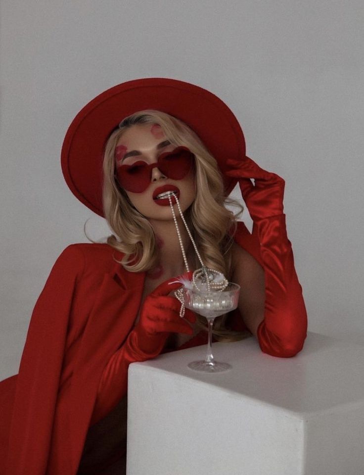 a woman in red is drinking from a wine glass with a straw sticking out of her mouth