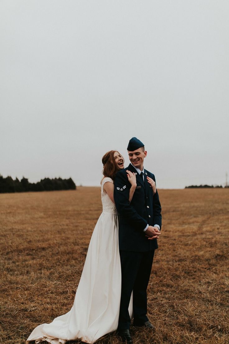 a bride and groom are standing in the middle of an open field with their arms around each other