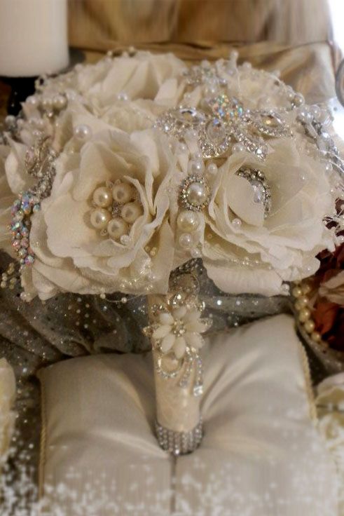 a bridal bouquet with white flowers and pearls sits on a pillow next to a candle