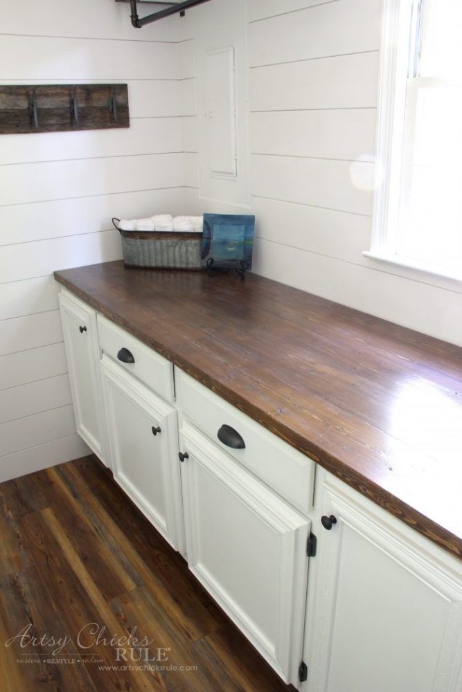 a white kitchen with wooden counter tops and cabinets in the corner, next to a window