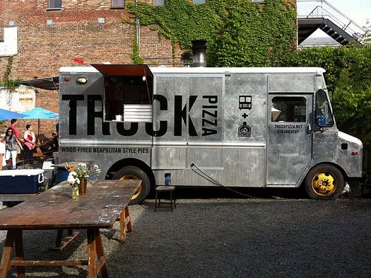 a food truck parked in front of a brick building with people standing around and eating