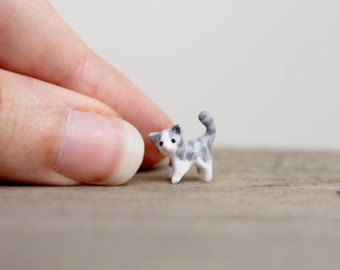 a tiny cat figurine sitting on top of a wooden table next to a person's finger