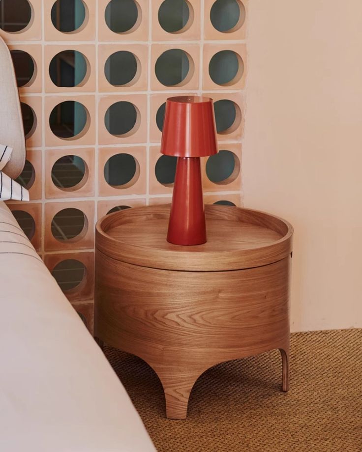 a nightstand with a red lamp on it next to a bed