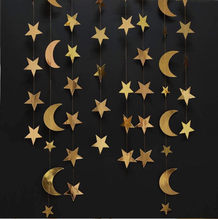 gold stars and crescents hanging from strings against a black wall with the moon in the middle