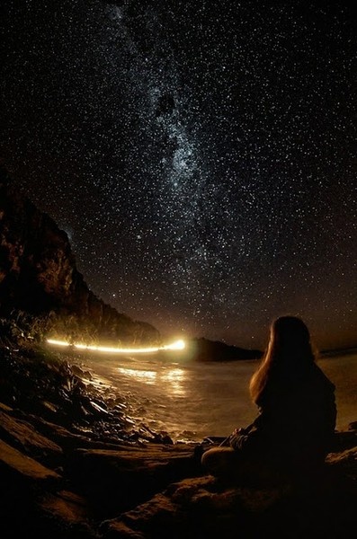 a woman sitting on the beach looking at the stars in the sky above her head