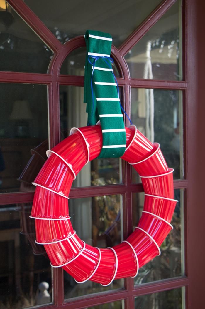 a red and green wreath hanging on the side of a door with ribbons attached to it