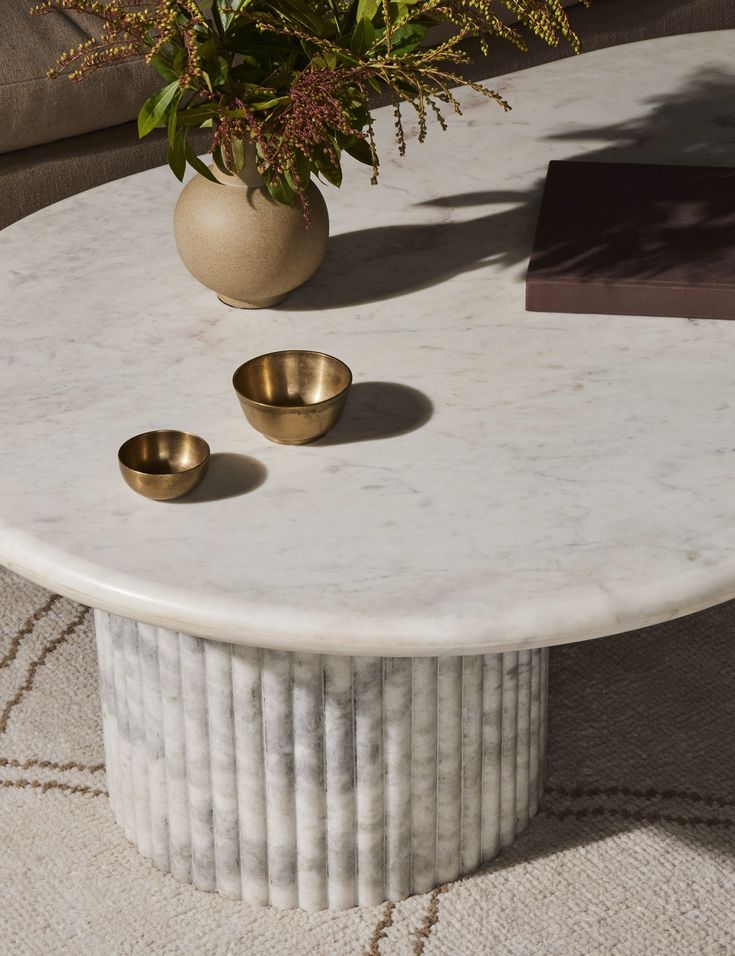 a white marble table with two gold cups on it and a vase filled with flowers