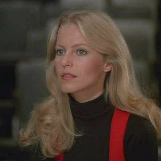 a woman with long blonde hair wearing a black turtle neck top and red suspenders