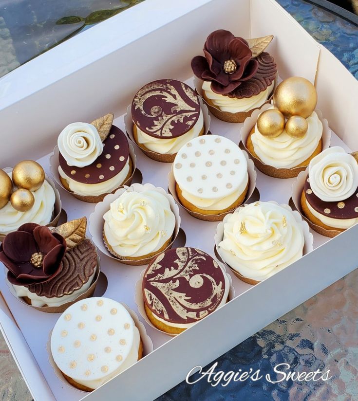 a box filled with lots of cupcakes covered in white frosting and gold decorations