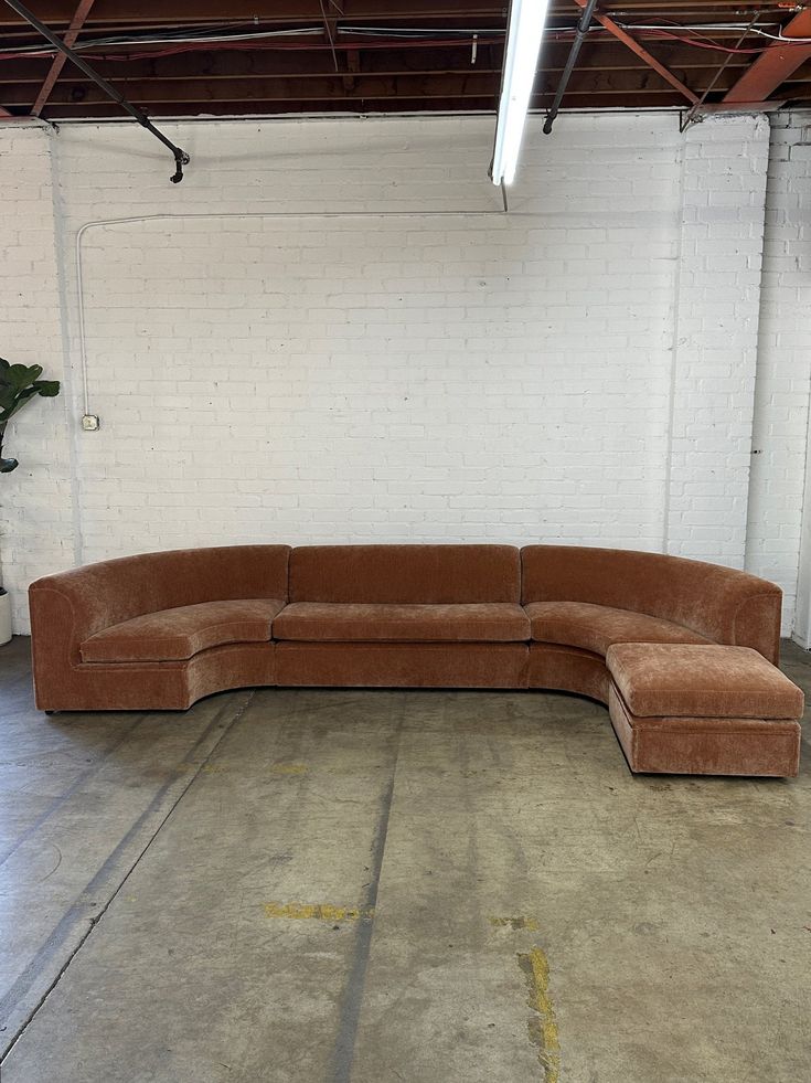 a large sectional couch sitting in an empty room next to a white brick wall with exposed pipes