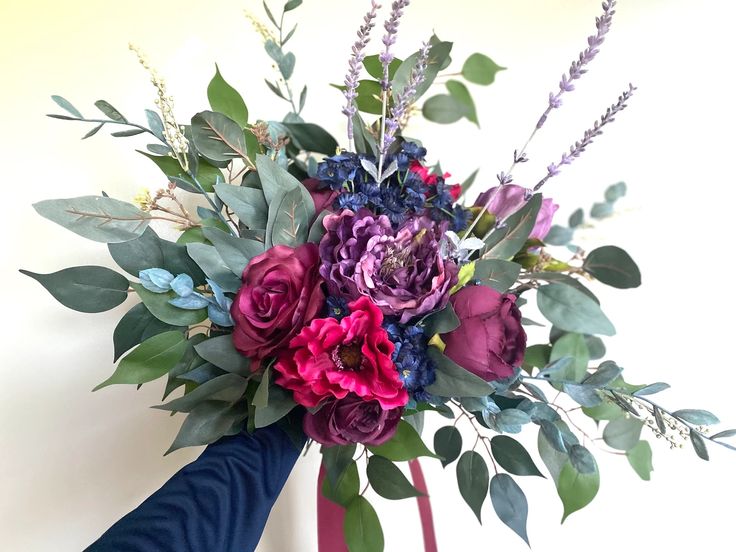 a bouquet of purple and red flowers on top of a blue vase filled with greenery