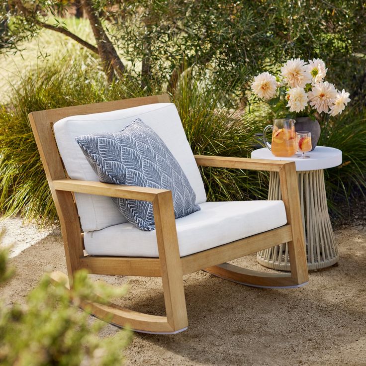 a wooden rocking chair sitting next to a table with flowers on it and a vase filled with oranges