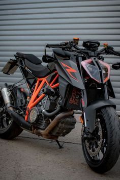 an orange and black motorcycle parked in front of a garage door