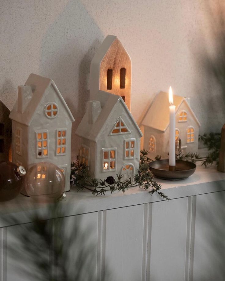 small white houses with lit candles sit on a mantle in front of a christmas tree